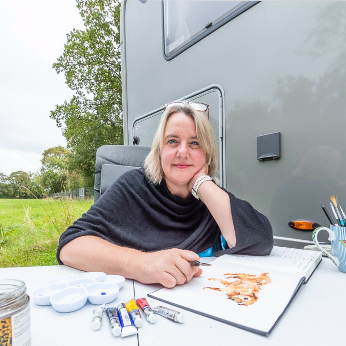 Artist Jo Scott sitting at a table with art supplies in front of her Hymer Motorhome