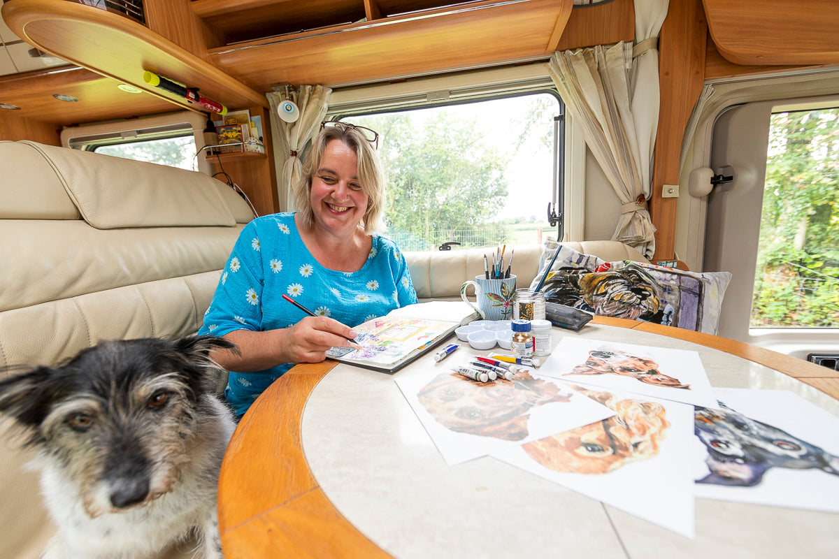 Artist Jo Scott photographed painting in her sketchbook inside her motorhome sat next to her dog Thomasina