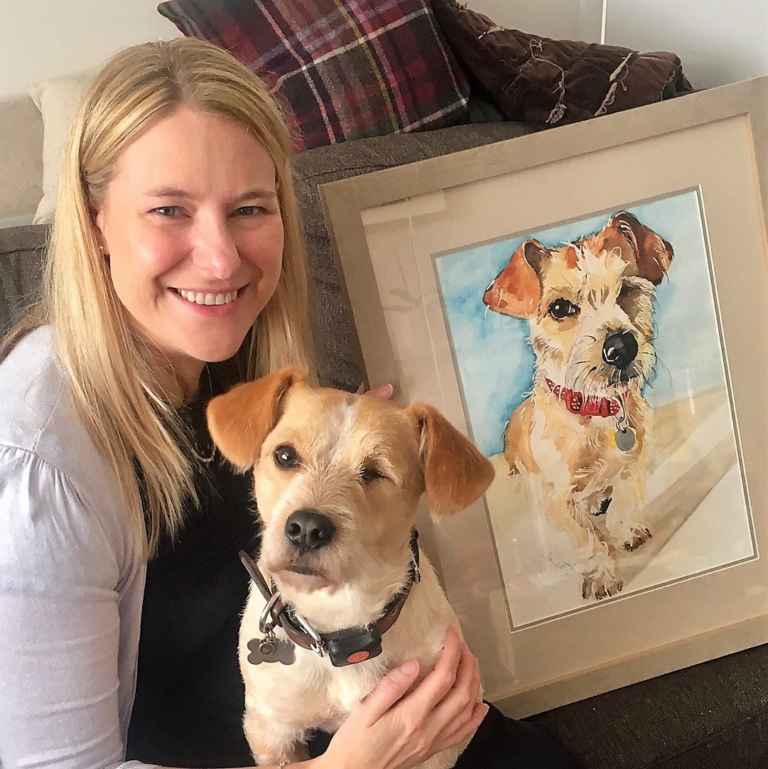 Photo of a smiling client posing with both a framed watercolour portrait and the dog that was painted